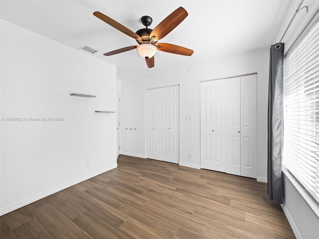 unfurnished bedroom featuring hardwood / wood-style floors, ceiling fan, and two closets