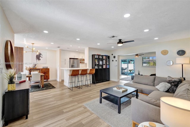 living room featuring a textured ceiling, ceiling fan with notable chandelier, and light hardwood / wood-style flooring