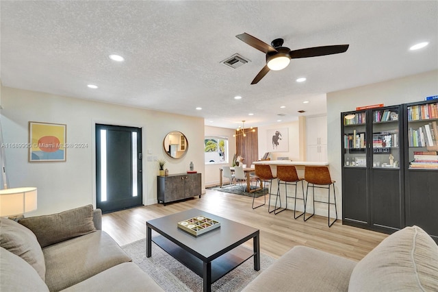 living room featuring light hardwood / wood-style flooring, ceiling fan with notable chandelier, and a textured ceiling