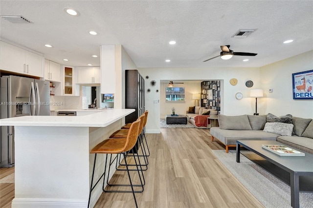 kitchen with stainless steel fridge, light hardwood / wood-style floors, a textured ceiling, a kitchen bar, and white cabinets