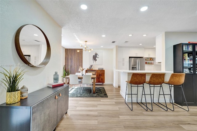 kitchen featuring stainless steel fridge, light wood-type flooring, a textured ceiling, white cabinets, and a chandelier