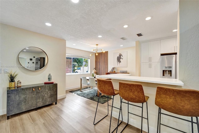 kitchen with a kitchen breakfast bar, kitchen peninsula, stainless steel fridge, light hardwood / wood-style floors, and white cabinetry