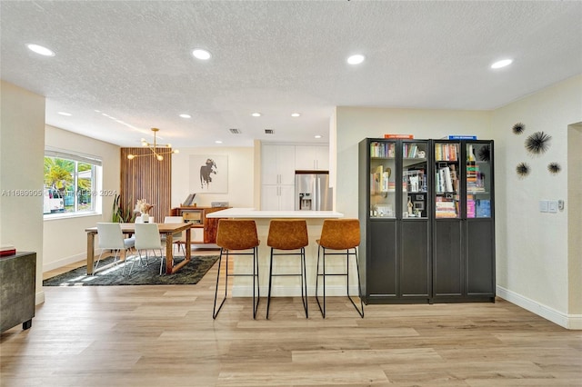 kitchen with a breakfast bar area, white cabinets, stainless steel refrigerator with ice dispenser, and light wood-type flooring