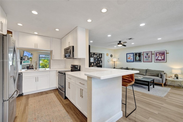 kitchen featuring a breakfast bar, kitchen peninsula, light wood-type flooring, appliances with stainless steel finishes, and white cabinetry