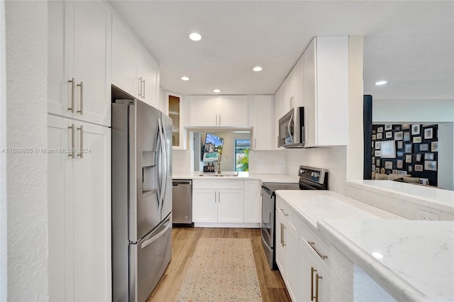 kitchen featuring light stone countertops, appliances with stainless steel finishes, light hardwood / wood-style flooring, and white cabinetry