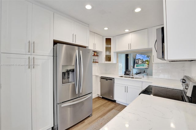 kitchen with sink, stainless steel appliances, light stone counters, white cabinets, and light wood-type flooring