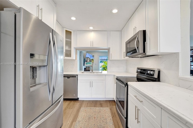 kitchen featuring sink, appliances with stainless steel finishes, light hardwood / wood-style floors, light stone counters, and white cabinetry