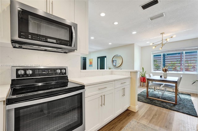 kitchen with light wood-type flooring, a textured ceiling, appliances with stainless steel finishes, a notable chandelier, and white cabinetry