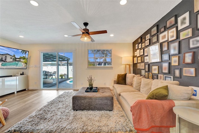 living room with a textured ceiling, light wood-type flooring, and ceiling fan