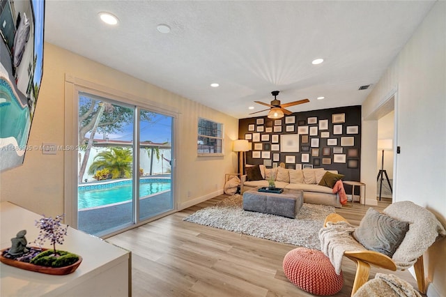 living room with a textured ceiling, light hardwood / wood-style floors, and ceiling fan