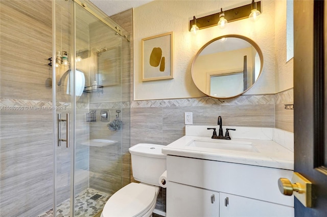 bathroom with vanity, toilet, a shower with door, and tile walls