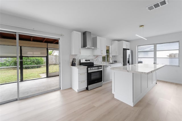 kitchen with decorative backsplash, hanging light fixtures, wall chimney range hood, white cabinetry, and appliances with stainless steel finishes