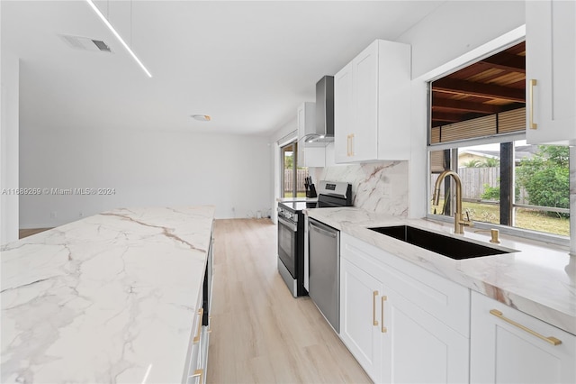 kitchen featuring wall chimney exhaust hood, sink, light stone counters, and appliances with stainless steel finishes