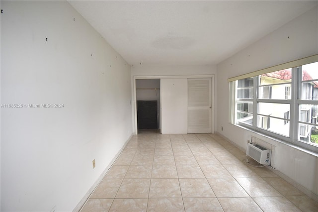 empty room with a wall mounted AC, a wealth of natural light, and light tile patterned floors