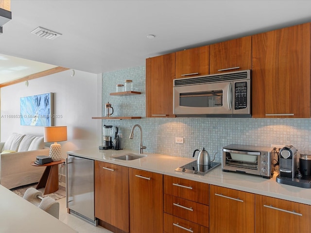 kitchen with a sink, fridge, brown cabinetry, stainless steel microwave, and visible vents