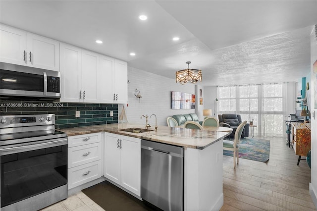 kitchen with kitchen peninsula, sink, white cabinetry, light wood-type flooring, and appliances with stainless steel finishes