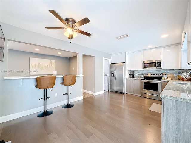 kitchen featuring a kitchen bar, white cabinets, light hardwood / wood-style flooring, tasteful backsplash, and appliances with stainless steel finishes