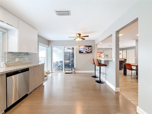 kitchen with white cabinetry, light stone counters, ceiling fan, stainless steel dishwasher, and light wood-type flooring