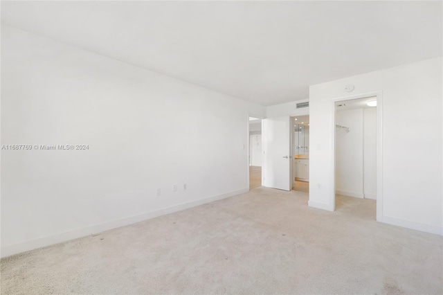 unfurnished bedroom featuring a closet, a walk in closet, and light carpet