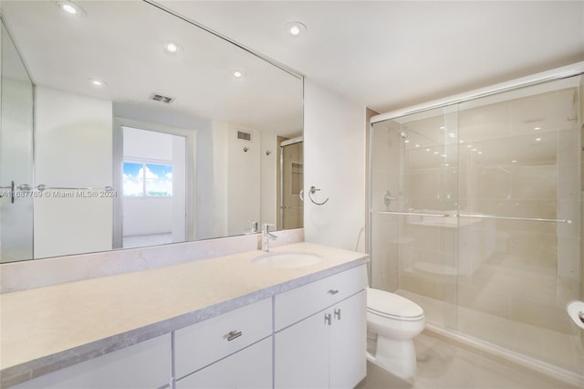 bathroom with toilet, vanity, and a shower with shower door