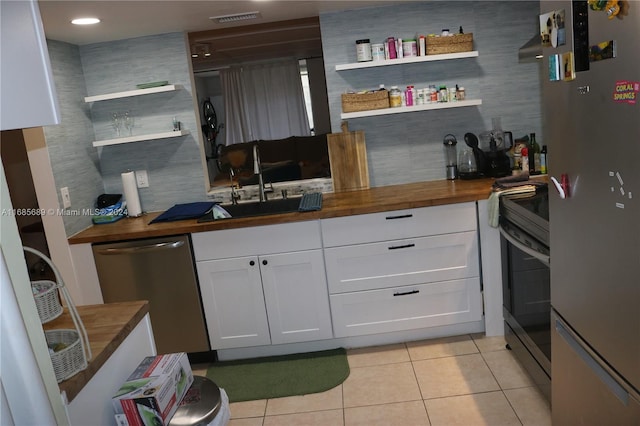 kitchen featuring butcher block countertops, appliances with stainless steel finishes, light tile patterned floors, and white cabinets