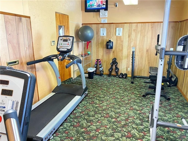 workout room with wood walls and dark colored carpet