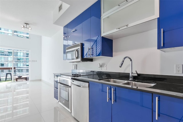 kitchen featuring appliances with stainless steel finishes, light tile patterned floors, sink, dark stone countertops, and blue cabinets