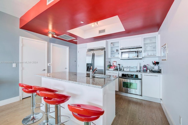 kitchen with light wood-type flooring, white cabinets, light stone counters, and stainless steel appliances