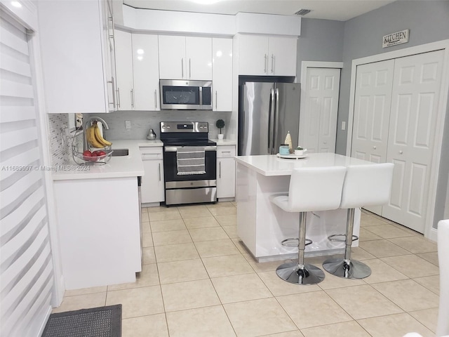 kitchen with a center island, light tile patterned flooring, backsplash, white cabinetry, and appliances with stainless steel finishes