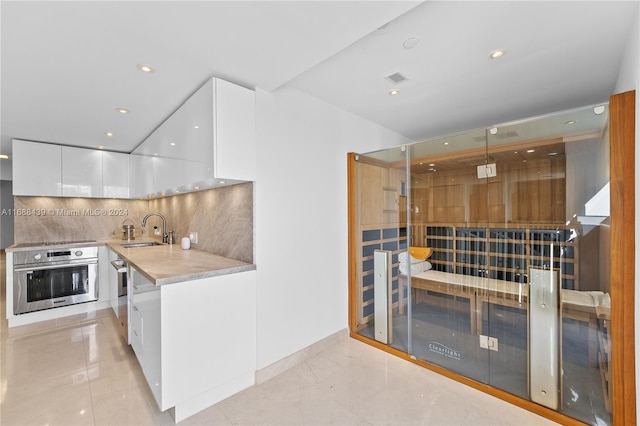 kitchen featuring decorative light fixtures, white cabinets, sink, tasteful backsplash, and stainless steel oven