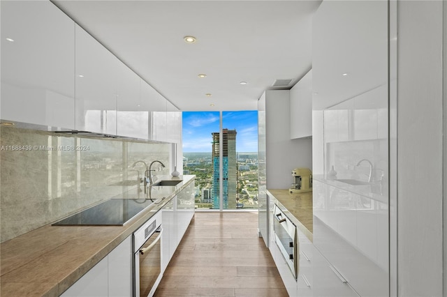 kitchen featuring black electric cooktop, sink, oven, white cabinetry, and light hardwood / wood-style flooring