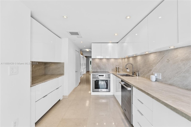 kitchen with sink, tasteful backsplash, light tile patterned floors, white cabinetry, and appliances with stainless steel finishes