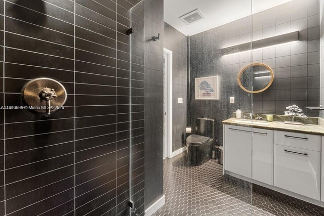 bathroom with vanity, a shower, tile patterned floors, toilet, and tile walls