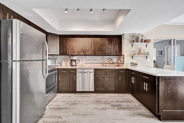 kitchen featuring kitchen peninsula, light hardwood / wood-style flooring, backsplash, a tray ceiling, and appliances with stainless steel finishes