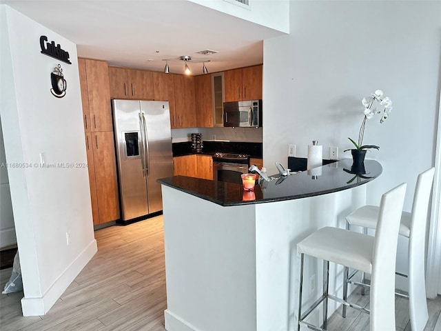 kitchen with a kitchen breakfast bar, kitchen peninsula, light hardwood / wood-style floors, and stainless steel appliances