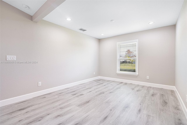 spare room with light wood-type flooring and beamed ceiling