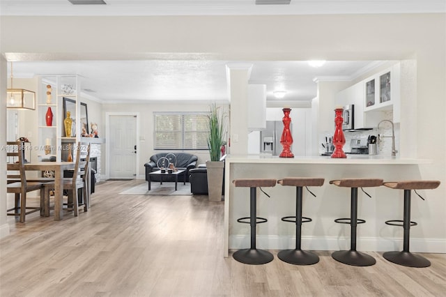 kitchen with light wood-type flooring, white cabinetry, a breakfast bar, and ornamental molding