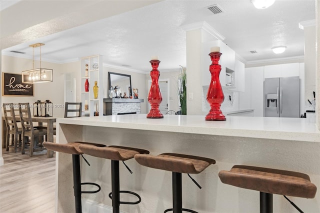 kitchen featuring light hardwood / wood-style floors, ornamental molding, white cabinetry, decorative light fixtures, and stainless steel fridge