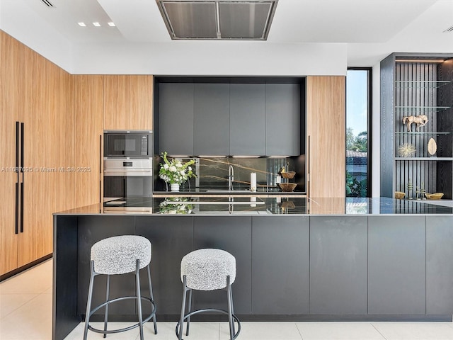 kitchen featuring stainless steel oven, black microwave, a breakfast bar area, and light tile patterned flooring