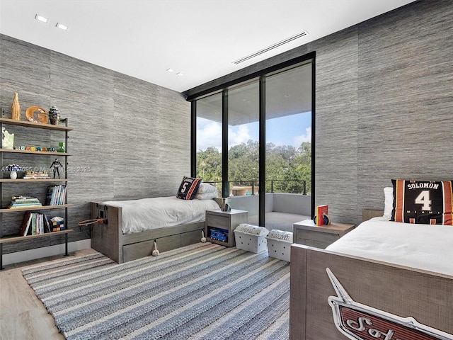 bedroom with wood-type flooring, access to exterior, a wall of windows, and tile walls