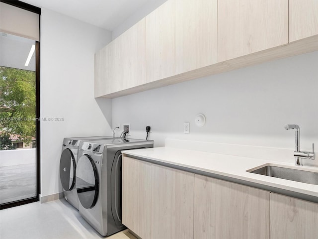 clothes washing area with sink, washer and clothes dryer, and cabinets