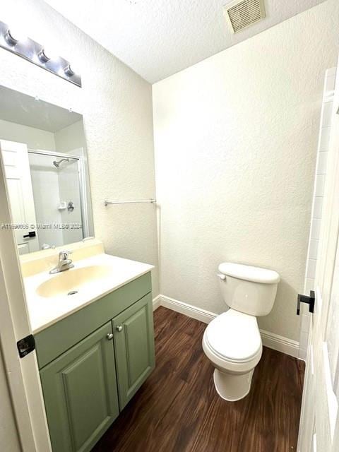 bathroom with a textured ceiling, hardwood / wood-style floors, vanity, a shower, and toilet