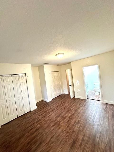 unfurnished bedroom featuring dark hardwood / wood-style flooring, a textured ceiling, two closets, and ensuite bath