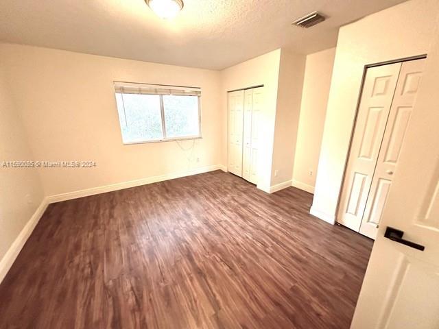 unfurnished bedroom featuring multiple closets, dark wood-type flooring, and a textured ceiling