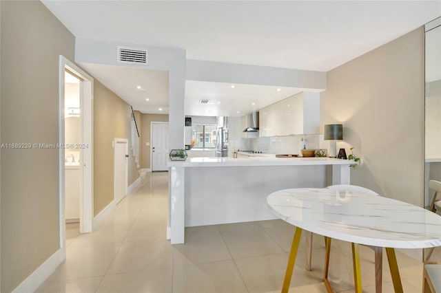 kitchen featuring kitchen peninsula, decorative backsplash, wall chimney exhaust hood, and white cabinets