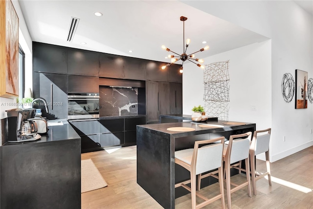 kitchen featuring a breakfast bar area, hanging light fixtures, oven, light hardwood / wood-style flooring, and a notable chandelier