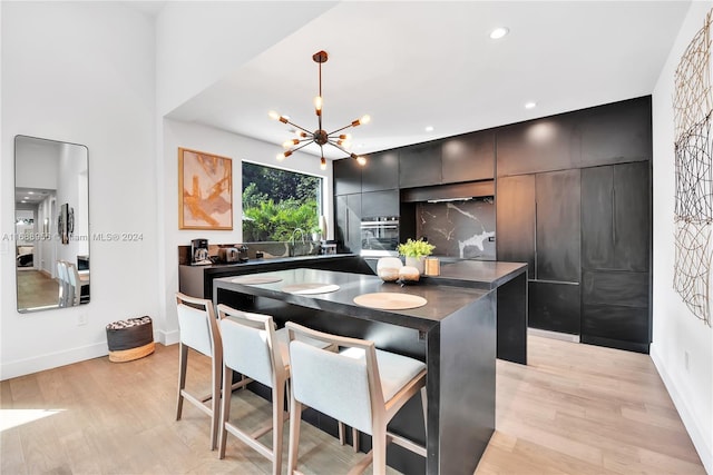 kitchen with a notable chandelier, pendant lighting, light hardwood / wood-style floors, oven, and a center island