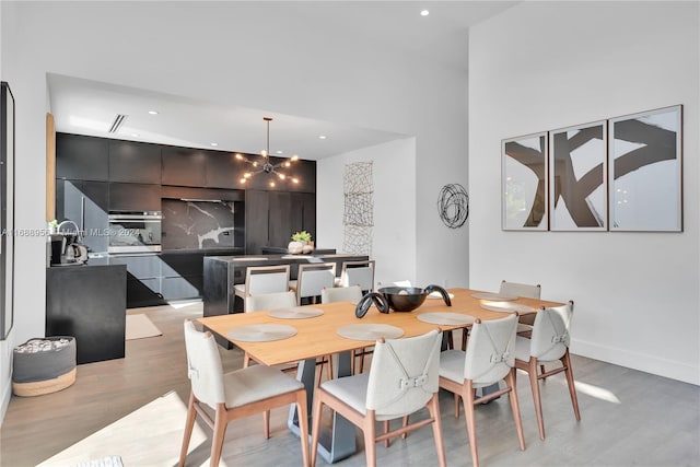 dining space featuring a towering ceiling, an inviting chandelier, and light hardwood / wood-style flooring