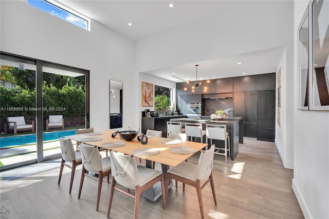 dining area featuring a towering ceiling, a chandelier, a healthy amount of sunlight, and light hardwood / wood-style flooring