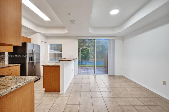 kitchen with light stone countertops, stainless steel fridge, kitchen peninsula, and a tray ceiling